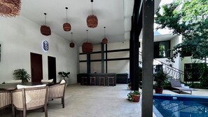 A modern outdoor seating area with wicker furniture, hanging wicker lamps, and a poolside lounge. - Modern 2BR Apartment in Tulum Great Location (Tulum)