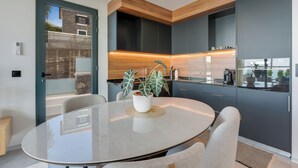 Une cuisine moderne avec des meubles de couleur sombre, une table ronde en verre et une plante en pot.