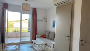Una sala de estar moderna con un sofá, una mesita y un banco. Hay una puerta corrediza de vidrio que da a un balcón.