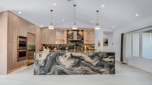 Een moderne keuken met een marmeren eiland, inbouwovens en hanglampen.