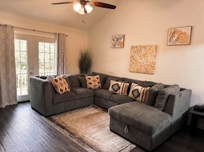 A living room with a sectional sofa, a ceiling fan, and artwork on the walls. - 3 Free Parking  Home in Auburn Al (Auburn)