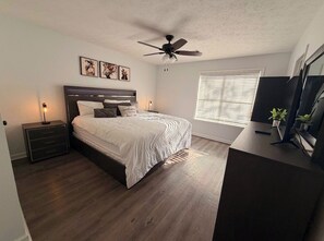 A bedroom with a bed, bedside tables, a ceiling fan, a window with blinds, and a desk with a plant. - 3 Free Parking  Home in Auburn Al (Auburn)
