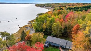 A house with a sloped roof, surrounded by autumn-colored trees, near a body of water. - Oceanfront Acadia Views Arcade Game Room Pets Ok (Surry)