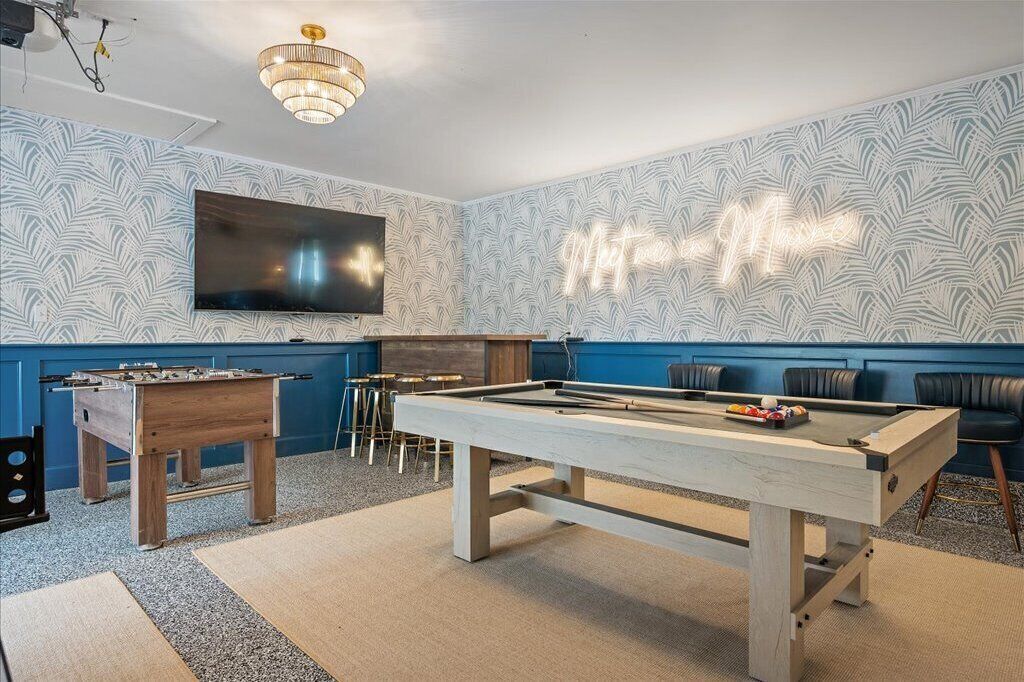 Una mesa de billar en una sala con pared azul, una mesa de fútbol de mesa y un televisor montado en la pared.