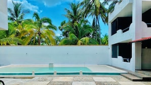 Une piscine dotée d  ’une terrasse carrelée, entourée de palmiers et surplombée d’un ciel dégagé.