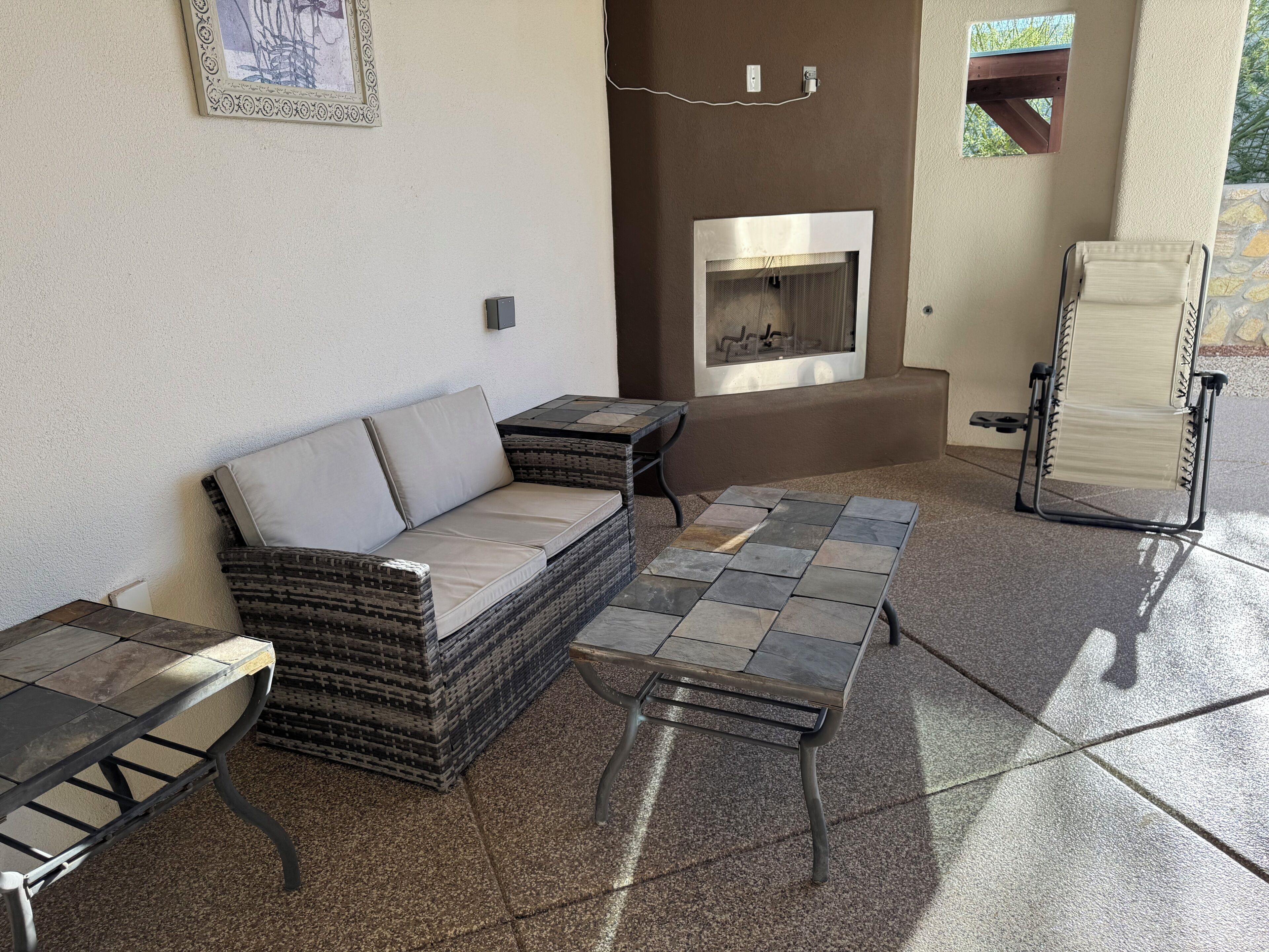 Eine Terrassenfläche mit einem Rattan-Sofa, einem Metalltisch, einer Feuerstelle und einem Stuhl.