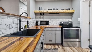 A compact kitchen with a wooden countertop, a built-in sink, a microwave, a stove, and a hanging pot rack. - Quiet Milton Retreat Close to Downtown & Water! (Milton)