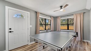 A room with a ping pong table, a ceiling fan, and large windows with curtains. - Quiet Milton Retreat Close to Downtown & Water! (Milton)