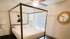 A four-poster bed in a bedroom with a ceiling fan, a bedside table with a lamp, and a round mirror on the wall. - Reagan 206: 2-bedroom apartment in  Dallas neighborhood (Dallas)