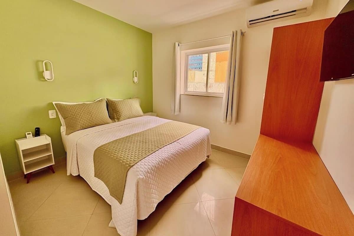 A bedroom with a bed, bedside table, and a window with curtains.