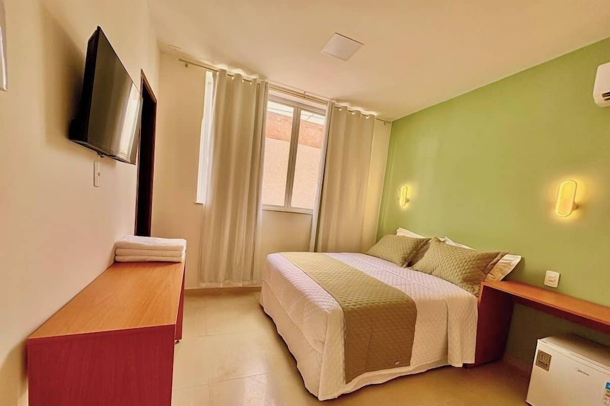 A hotel room with a bed, a desk, a TV, and a mini-fridge.