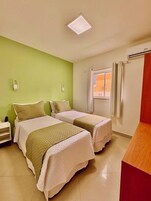 Habitación de hotel con dos camas, un escritorio pequeño, una ventana con cortinas e iluminación en el techo.