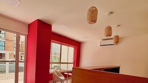 Una zona de recepción moderna con un muro decorado en rojo, un mostrador de madera y un área de descanso con una silla blanca y una pequeña mesa redonda.