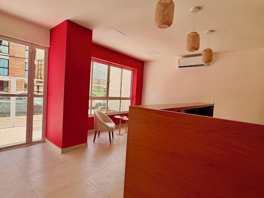 A modern reception area with a red accent wall, a wooden reception desk, and a seating area with a white chair and a small round table.