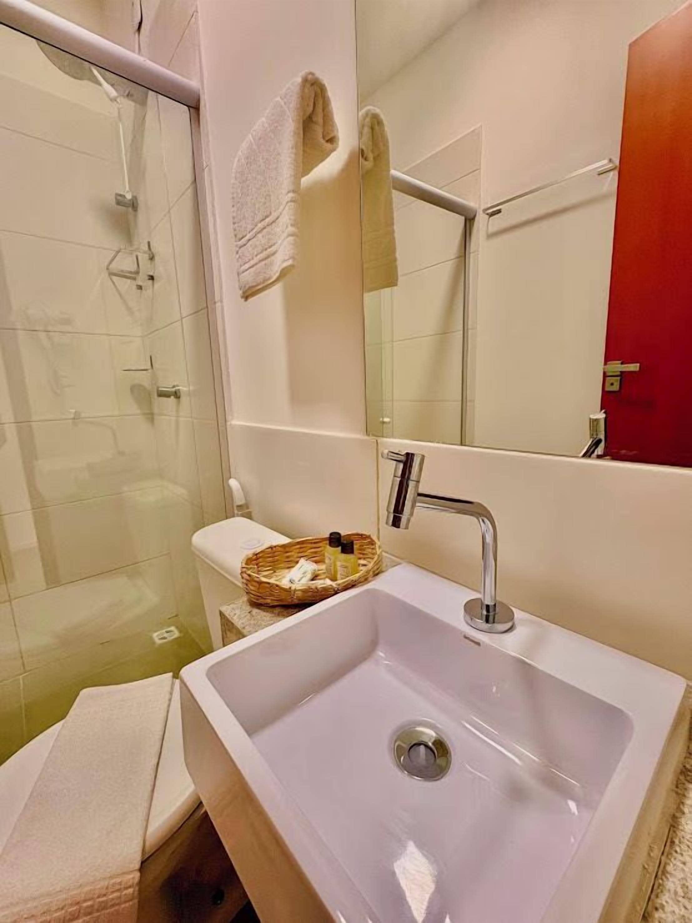 Ein Badezimmer mit weißem Waschbecken, einer Duschkabine aus Glas, einer Toilette und einem Spiegel.