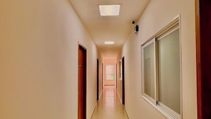 Un largo y estrecho pasillo con suelo de baldosas, puertas a ambos lados y un ventanal grande a la derecha.