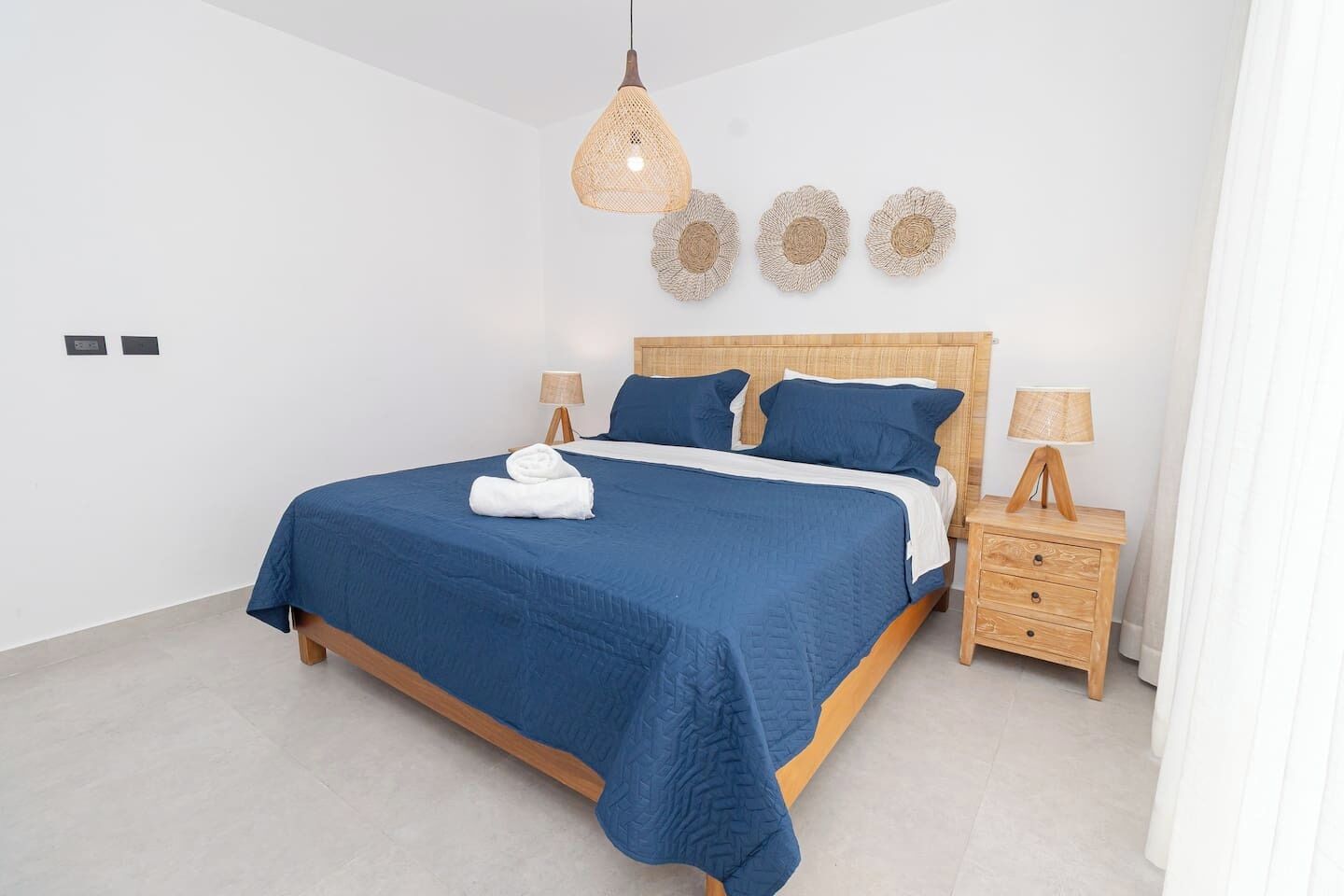 A bedroom with a large bed, two bedside tables, a hanging light fixture, and three wall-mounted decorative items.
