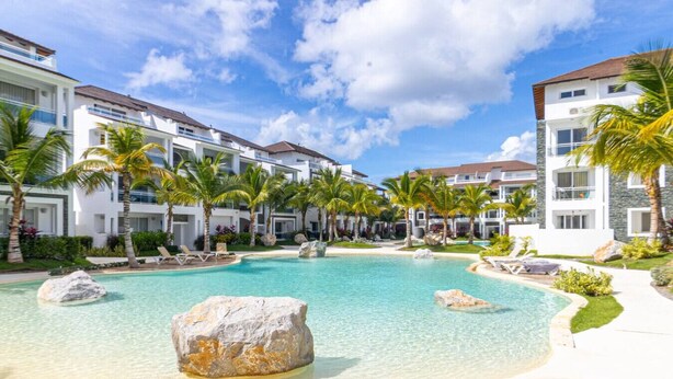 A resort with a large pool surrounded by palm trees and modern buildings. - Elegant 1-BD Luxury Escape in Paradise in Estrella (Dominicus)