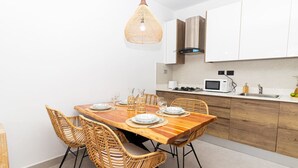 A modern kitchen with a wooden dining table, wicker chairs, and white cabinets. - Elegant 1-BD Luxury Escape in Paradise in Estrella (Dominicus)