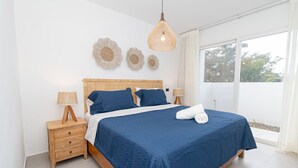 A bedroom with a large bed, wooden headboard, two bedside tables with lamps, and a window with curtains. - Elegant 1-BD Luxury Escape in Paradise in Estrella (Dominicus)