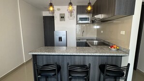 Une cuisine moderne dotée d’un îlot central, de trois tabourets de bar, d’un four encastré et de luminaires suspendus.