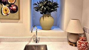 A modern kitchen with a stainless steel sink, a potted plant, a decorative lamp, and a framed artwork on the wall. - Vibrant 4BR | 2Bath | Home |High-end |Cntr Cheltenham |All stays | Parking incl (Cheltenham)