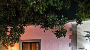 Ein gemütlicher Sitzbereich im Freien mit einer Bank und einem Tisch, umgeben von Blumentöpfen und einer rosa Wand.