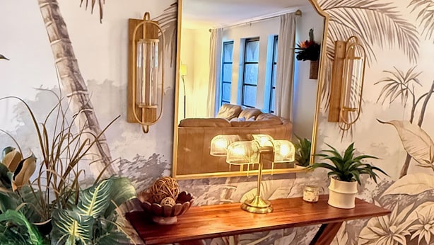 A room with a wooden console table, a large mirror, and a tropical-themed mural on the wall. - Tropical Southern Exposure Heated Pool Home in the Heart of Cape Coral (Cape Coral)