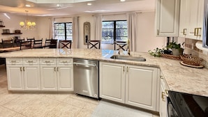 A modern kitchen with a central island, stainless steel dishwasher, and white cabinetry. - Tropical Southern Exposure Heated Pool Home in the Heart of Cape Coral (Cape Coral)