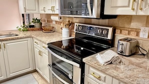 A modern kitchen with white cabinets, stainless steel appliances, and a granite countertop. - Tropical Southern Exposure Heated Pool Home in the Heart of Cape Coral (Cape Coral)
