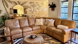 A living room with a brown leather sectional sofa, a zebra-patterned rug, and a woven ottoman. - Tropical Southern Exposure Heated Pool Home in the Heart of Cape Coral (Cape Coral)