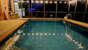 A swimming pool with a glass ceiling, surrounded by a wooden deck and a small seating area. - Tropical Southern Exposure Heated Pool Home in the Heart of Cape Coral (Cape Coral)
