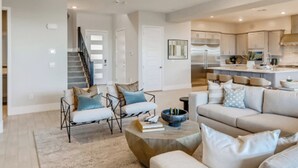A modern living room with a sofa, coffee table, and a staircase leading to another level. - Luxe Desert Escape w/ Strip View - 360° Las Vegas Strip & Mountain Views (Henderson)