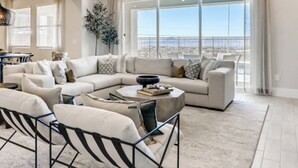 A spacious living room with a large sectional sofa, a coffee table, and a view of the city through large windows. - Luxe Desert Escape w/ Strip View - 360° Las Vegas Strip & Mountain Views (Henderson)