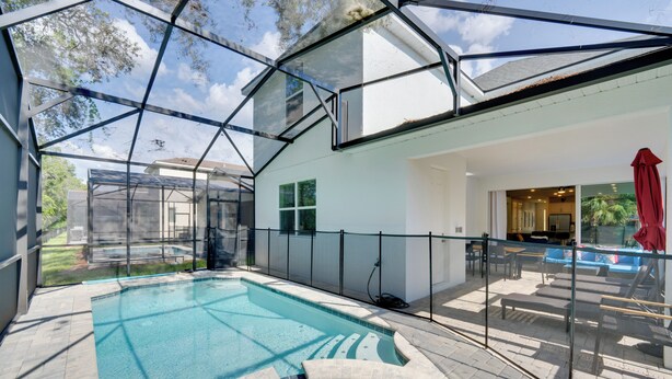 Ein modernes Haus mit einem überdachten Pool, einer Terrasse mit Gartenmöbeln und Blick auf den Garten.