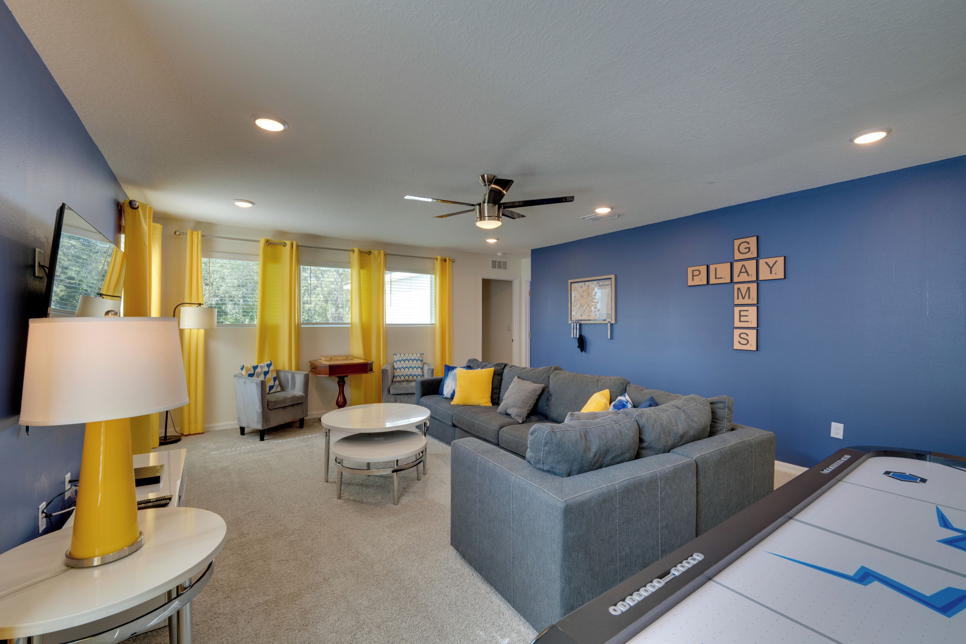 A modern living room with a gray sectional sofa, yellow curtains, and a pool table.