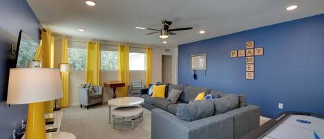 A modern living room with a gray sectional sofa, yellow curtains, and a pool table.