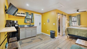 Una habitación compacta con kitchenette, cama, una mesita y ventilador de techo.