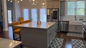 Een moderne keuken met een centraal eiland, roestvrijstalen apparatuur en een eethoek met gele stoelen.