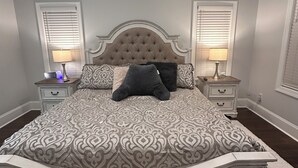 Een slaapkamer met een groot bed, twee nachtkastjes, een bankje en een raam met jaloezieën.