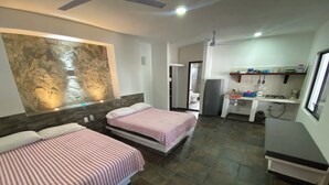 Een kamer met twee bedden, een stenen muur, een kitchenette en een badkamer.