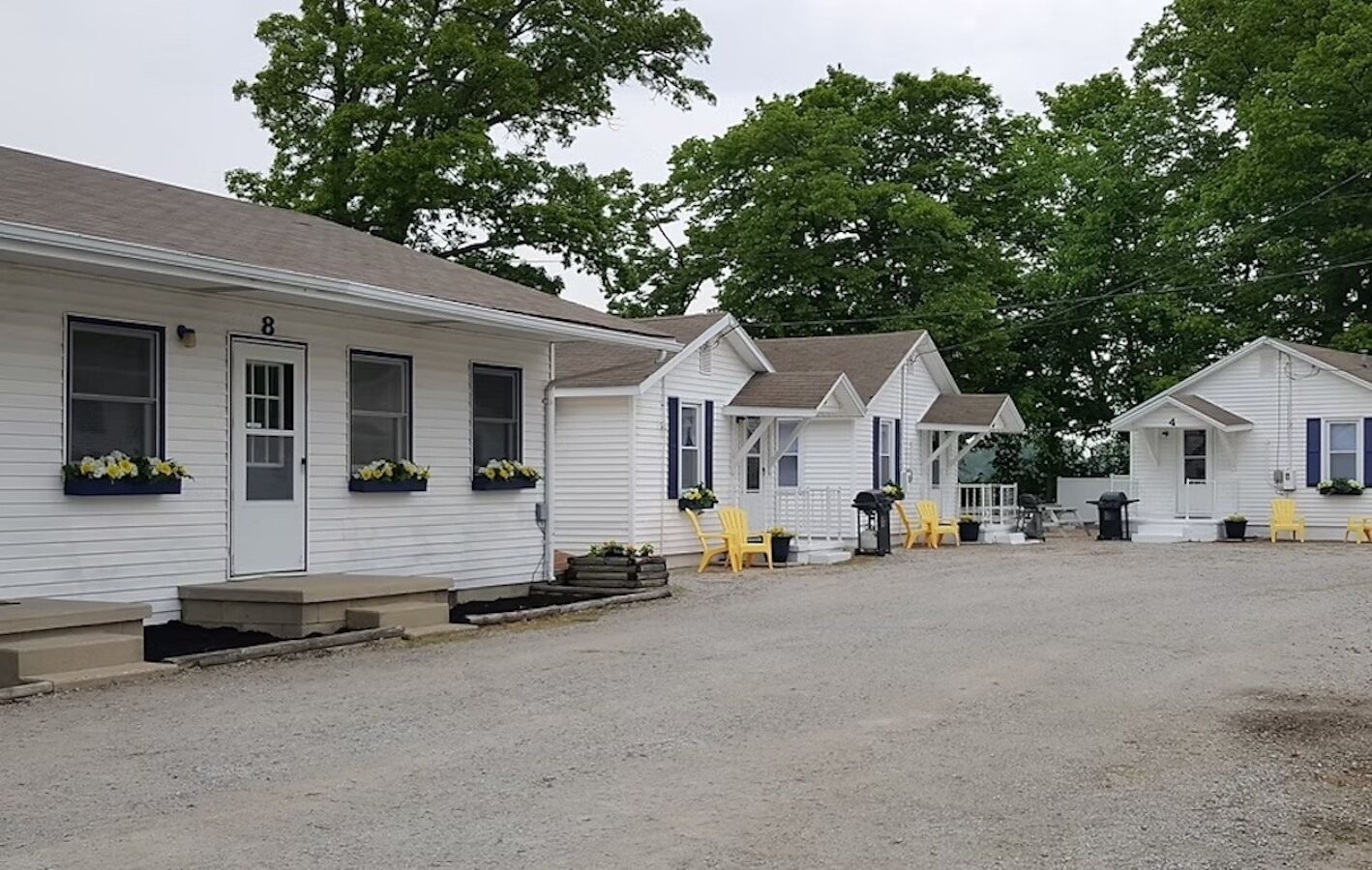 A row of white mobile homes with numbered doors, outdoor seating, and flower boxes.