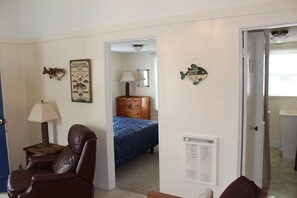 A room with a brown leather chair, a bed with a blue bedspread, a wooden dresser, a lamp, and wall decorations including a welcome sign and a fish sign. - Dockside Lake Resort (Monticello)