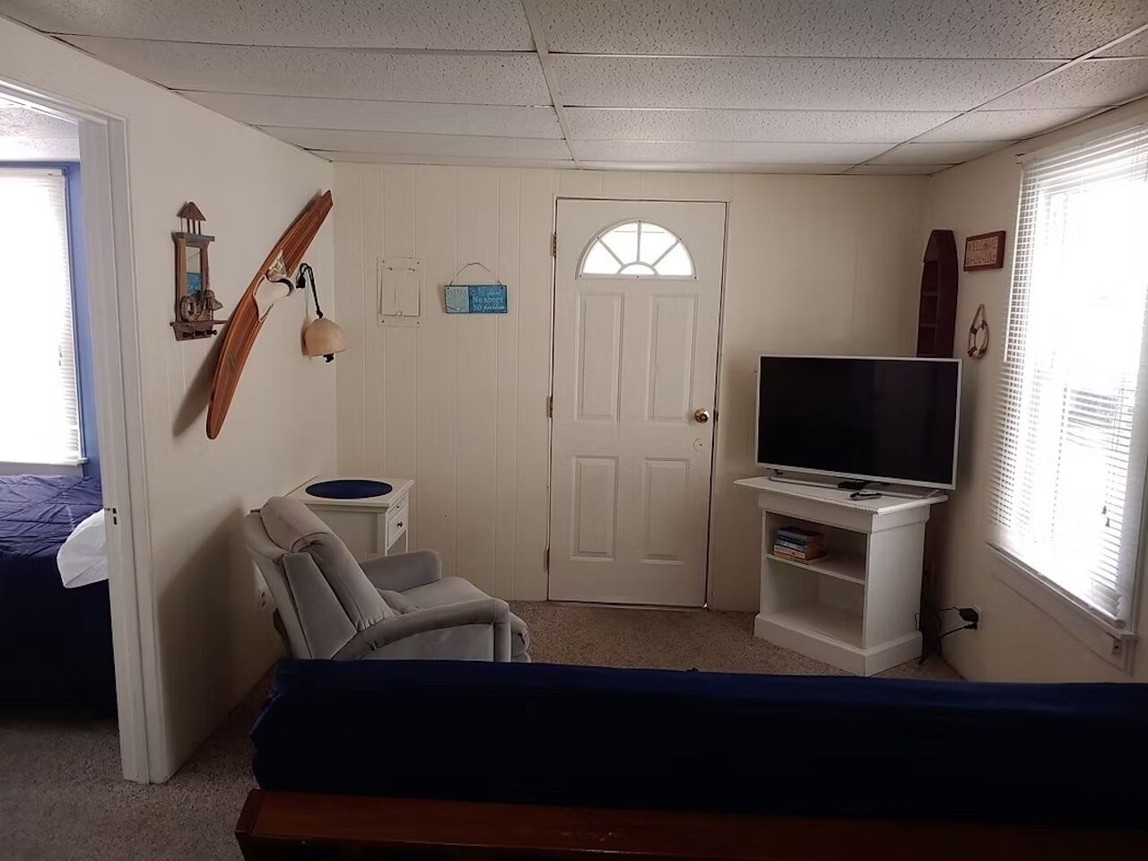 A room with a bed, a television on a stand, a chair, and a door with a window.