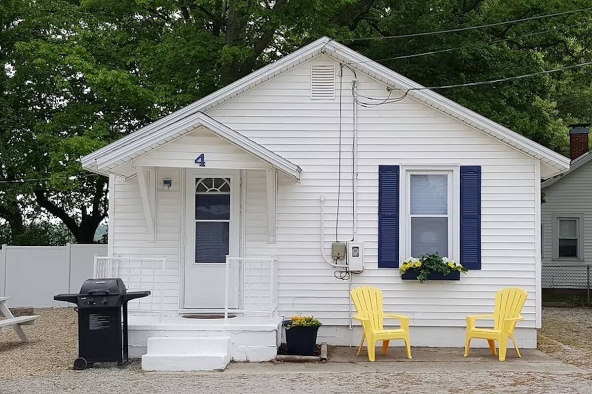 A small white house with a number 4 on the door, two yellow chairs outside, and a grill on the left.
