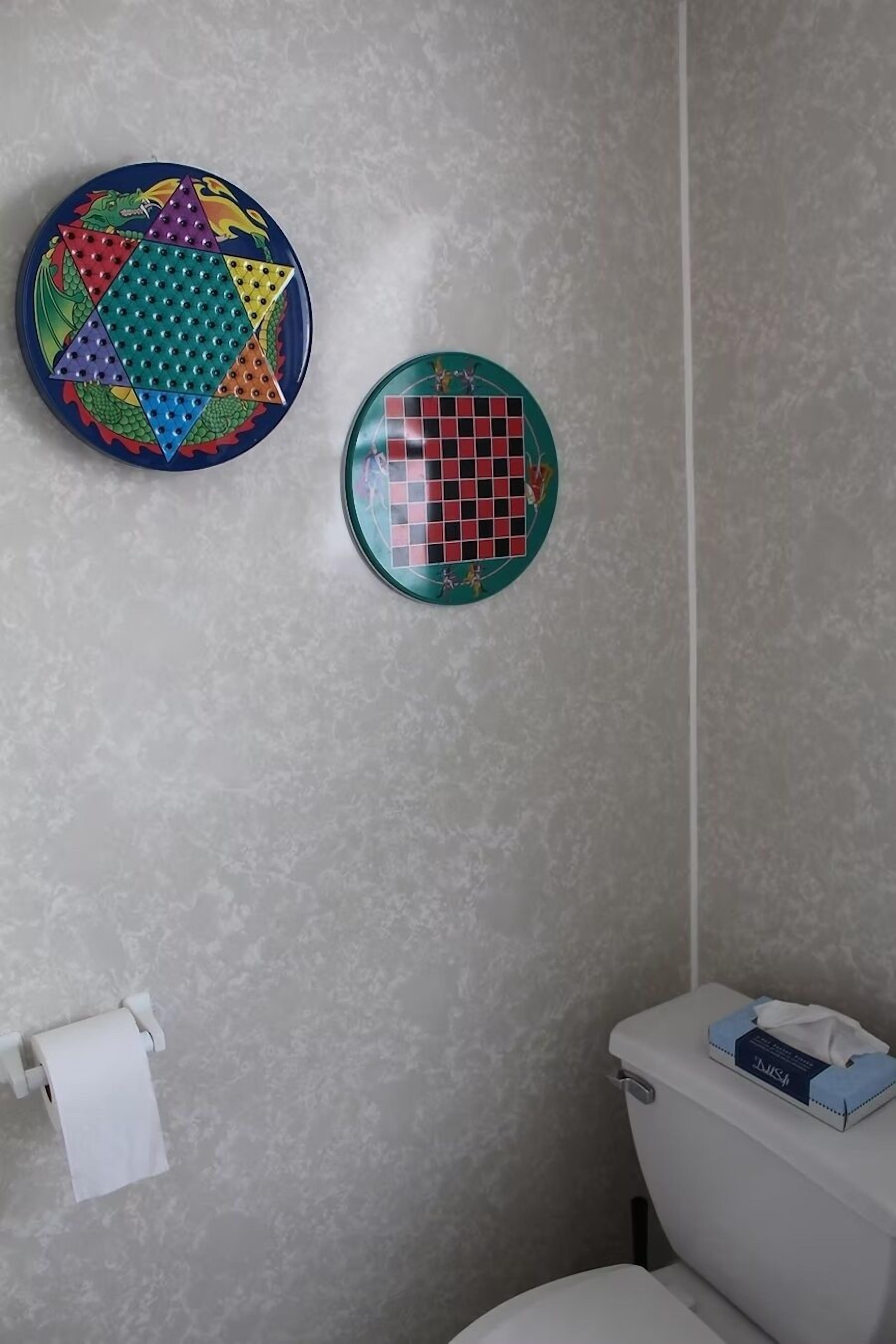 Un baño con inodoro, un dispensador de papel higiénico y dos placas decorativas en la pared.