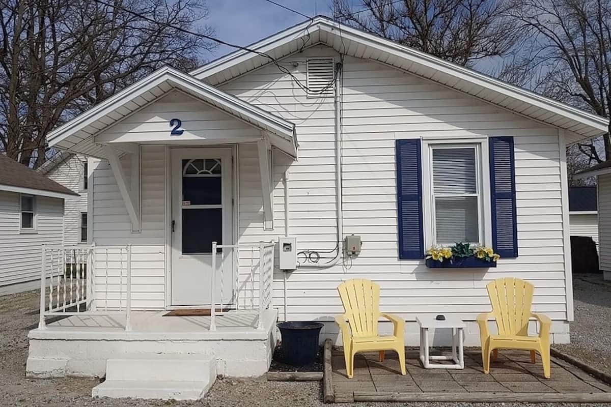 A small white house with a number '2' on the front, a porch with steps, and two yellow chairs outside.