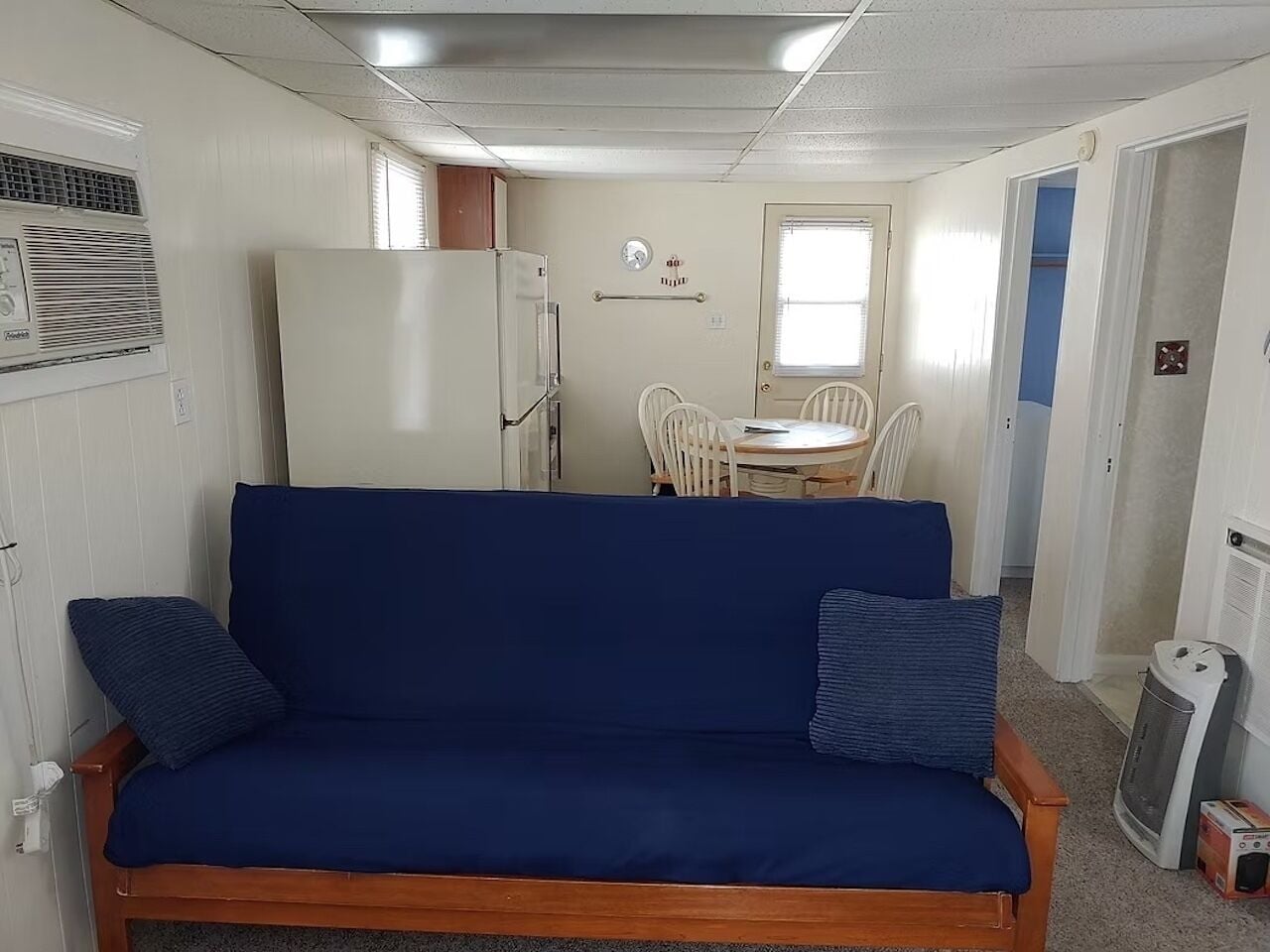 A compact room with a blue sofa, a small dining table, and a white refrigerator.