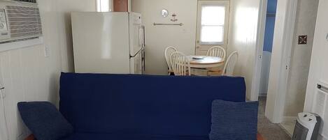 A compact room with a blue sofa, a small dining table, and a white refrigerator.
