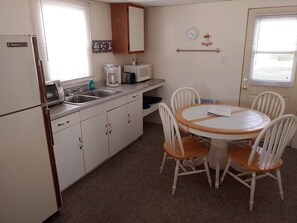 A compact kitchen with a sink, microwave, and coffee maker. There is a round table with four chairs and a small window with blinds. - Dockside Lake Resort (Monticello)